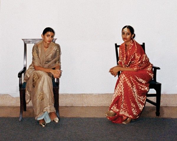 Two women sit in chairs wearing saris