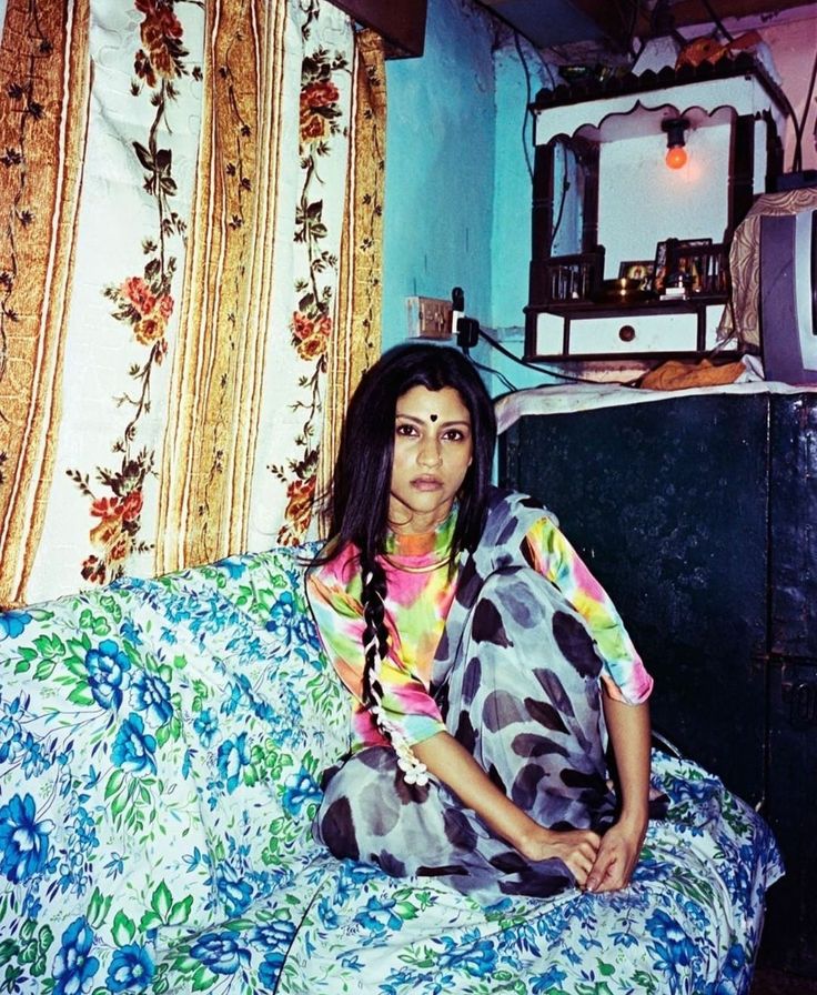 A woman stares into the camera while sitting on a couch in Indian style clothing
