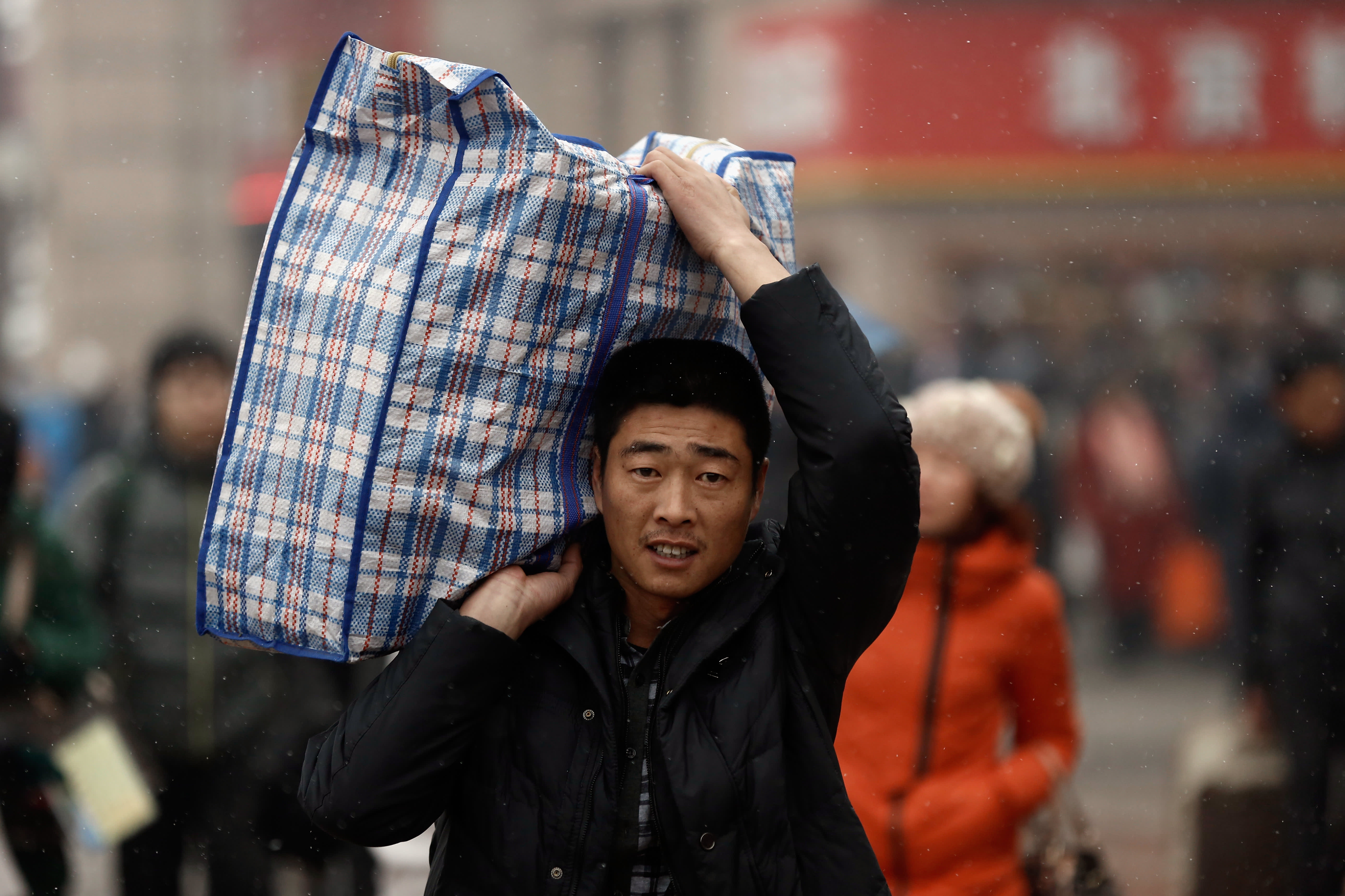 A man stares into the camera while holding a plaid bag over his shoulder