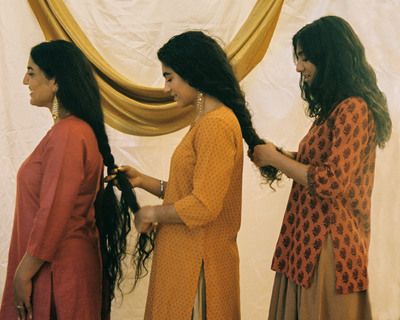 Three women braid each other's hair in a line